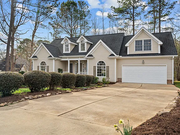 Angled exterior view of the tan home with layered gables, dormers, and a broad driveway