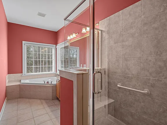 Bathroom with a glass shower, corner soaking tub, broad window, and warm coral walls