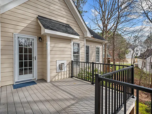Rear composite deck with black railings, French doors, and wooded neighborhood views