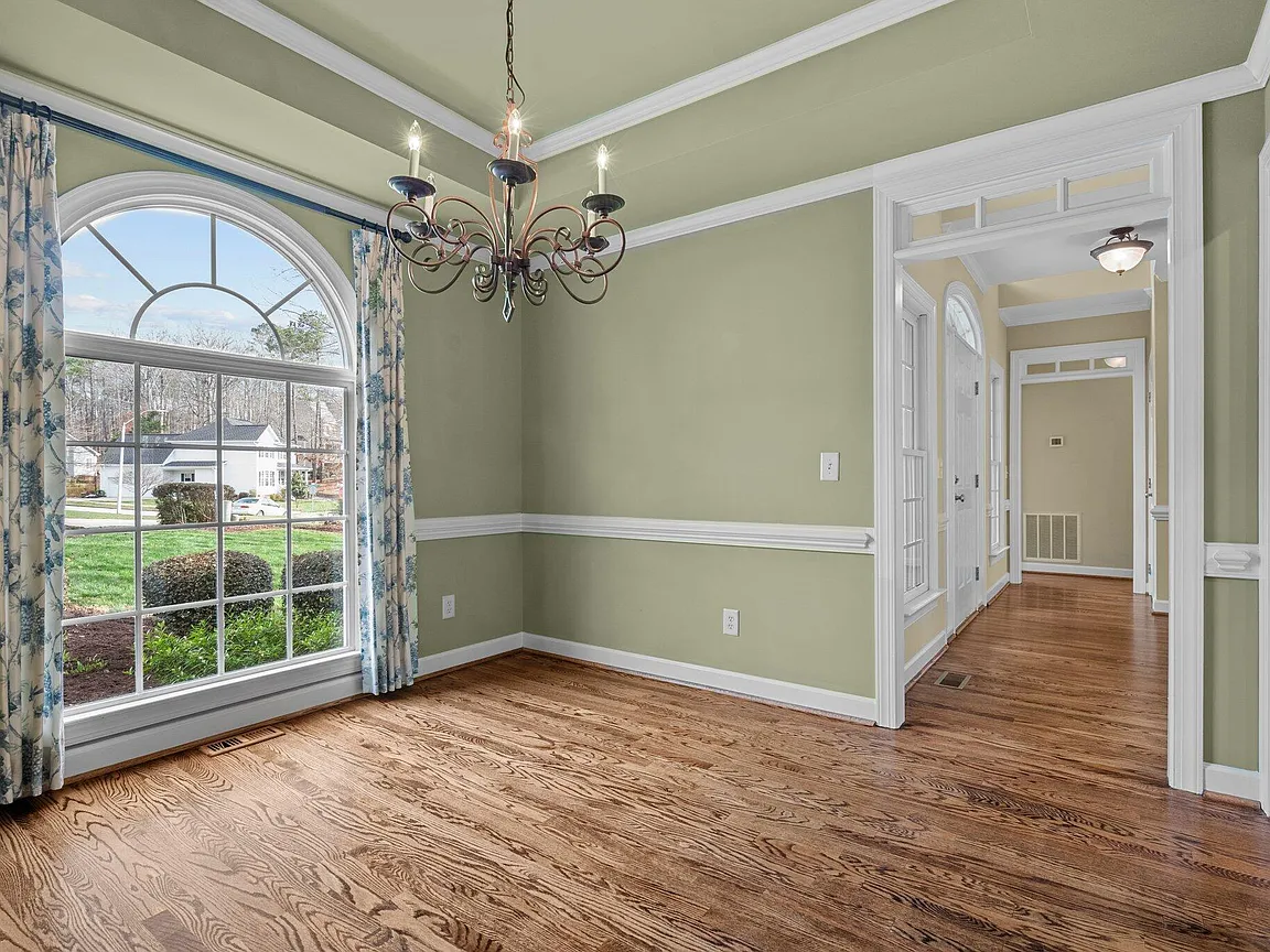 Formal dining room with a tall arched window, chandelier, white trim, and warm wood flooring