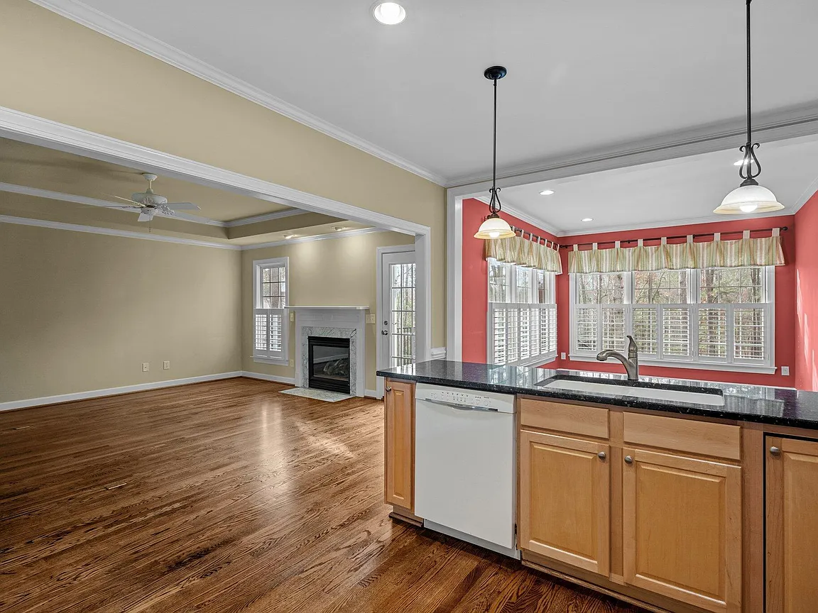 Kitchen and breakfast area with warm wood cabinetry, dark counters, pendant lighting, and broad windows