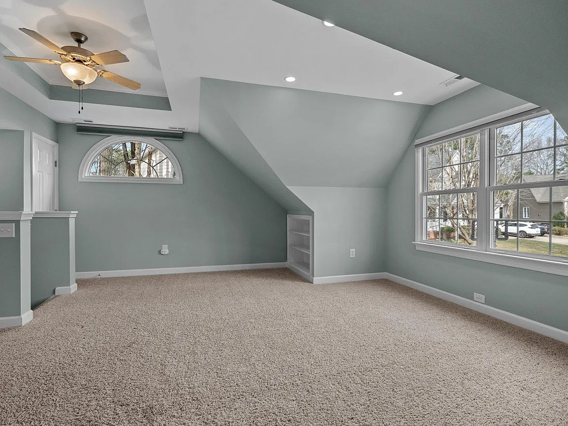 Spacious loft with sculpted ceilings, broad windows, an arched window, and built-in shelving
