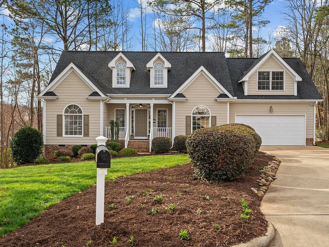 Tan one-and-a-half-story home with arched windows, dormers, a covered porch, and an attached garage