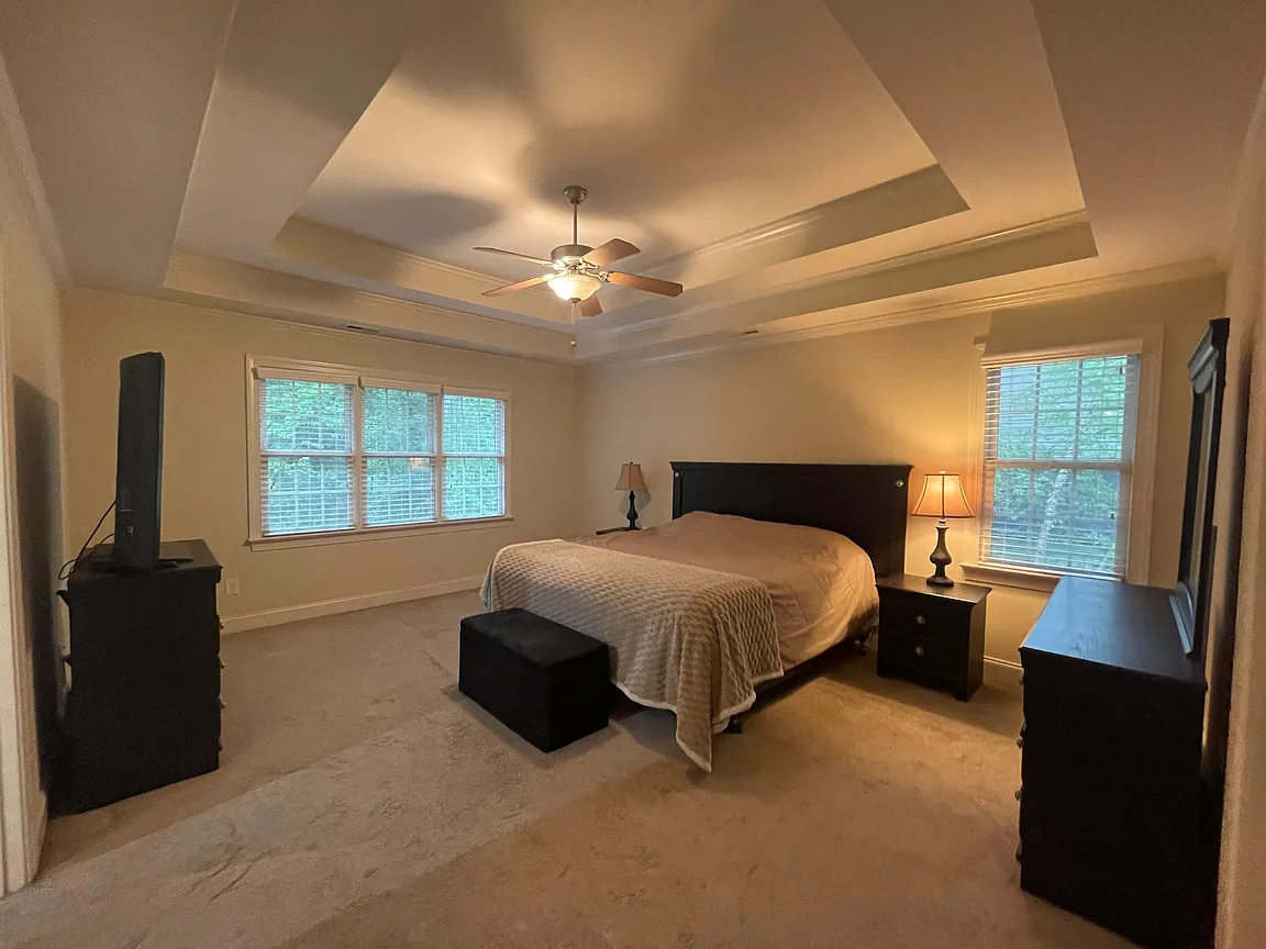 Primary bedroom with a tray ceiling, soft carpeting, and windows overlooking the trees