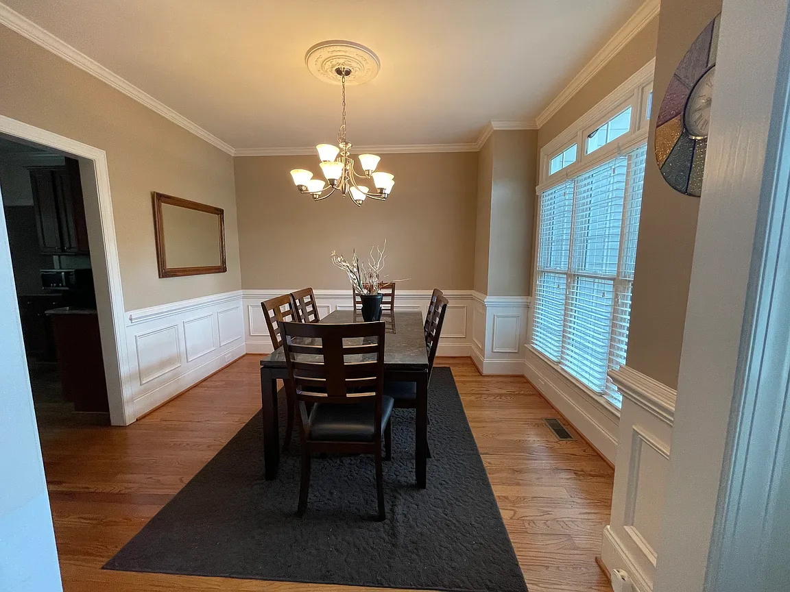 Dining room with warm wood flooring, white paneled wainscoting, and a broad window