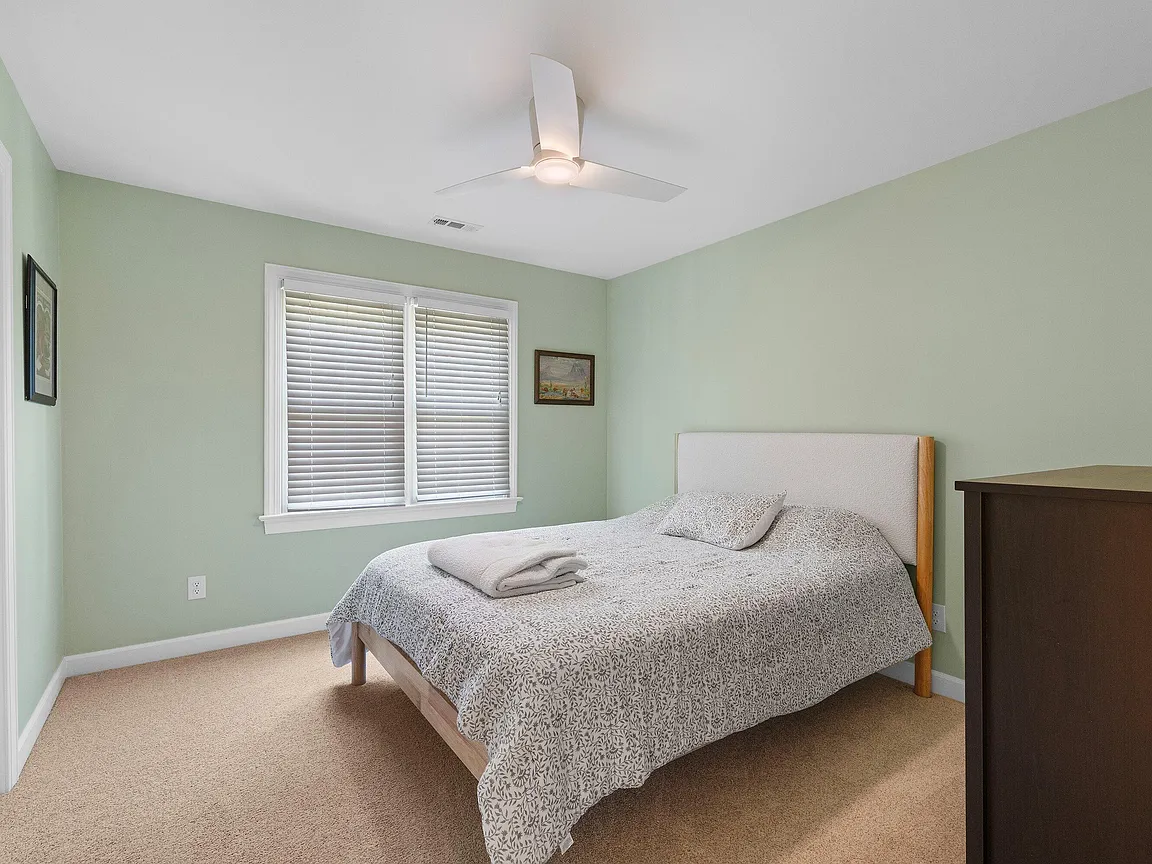 Soft green bedroom with a modern ceiling fan, neutral carpet, and a broad window