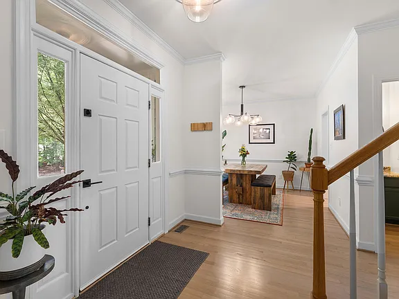 Bright entry hall with white trim, warm wood flooring, and a view into the dining room
