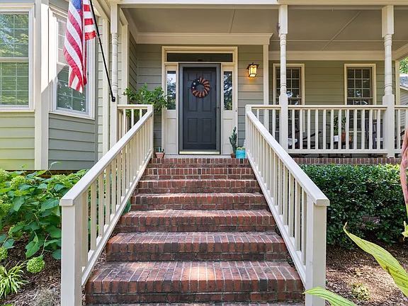 Brick front steps leading to a covered porch with white railings and a dark entry door