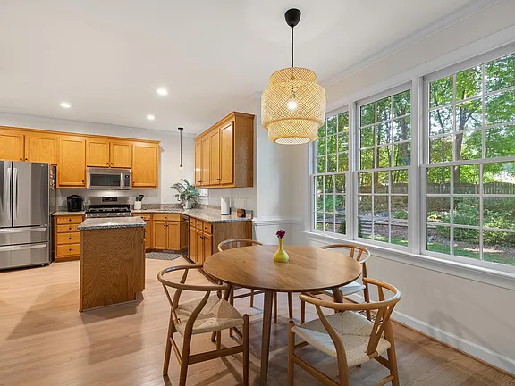 Kitchen and breakfast area with warm wood cabinetry, broad windows, and light wood flooring