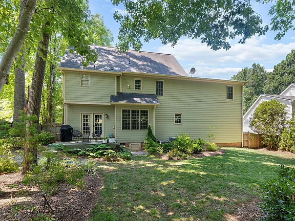 Rear exterior of the green two-story home with a patio and wooded backyard