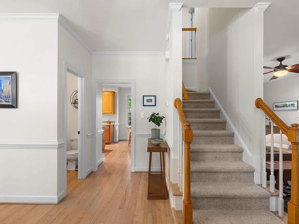 Open stair hall with warm wood flooring, white trim, and a carpeted staircase