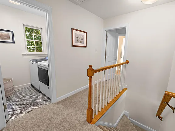 Upper stair landing with white spindles, warm wood railing, and an adjacent laundry room