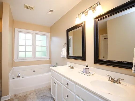 Bright bathroom with a double white vanity, soaking tub, and dark framed mirrors