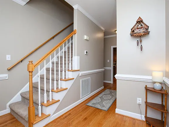 Entry hall with warm wood flooring, a carpeted staircase, and white railing