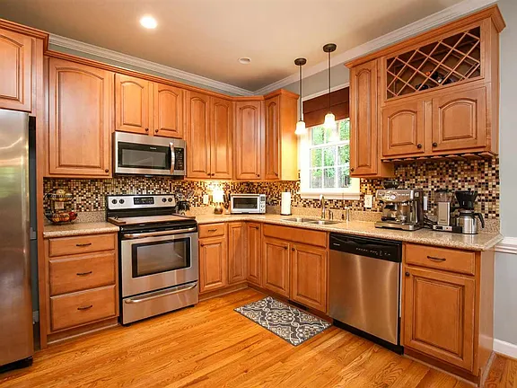 Warm wood kitchen with stainless appliances, mosaic backsplash, and a window over the sink