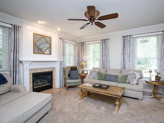 Living room with a white fireplace, broad windows, and soft neutral furnishings