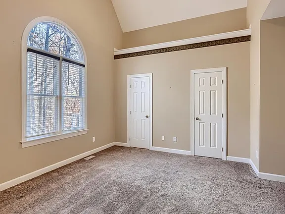 Vaulted bedroom with an arched window, neutral carpet, and soft beige walls
