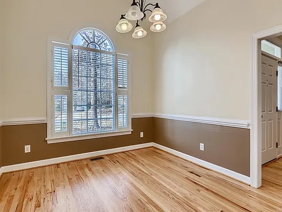 Dining room with an arched window, warm wood flooring, two-tone walls, and a chandelier