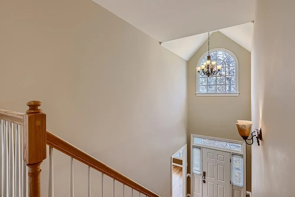 View from the upper staircase toward a tall arched window and bright front entry