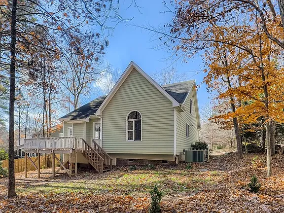 Rear exterior of the sage green home with a raised wood deck and wooded backyard