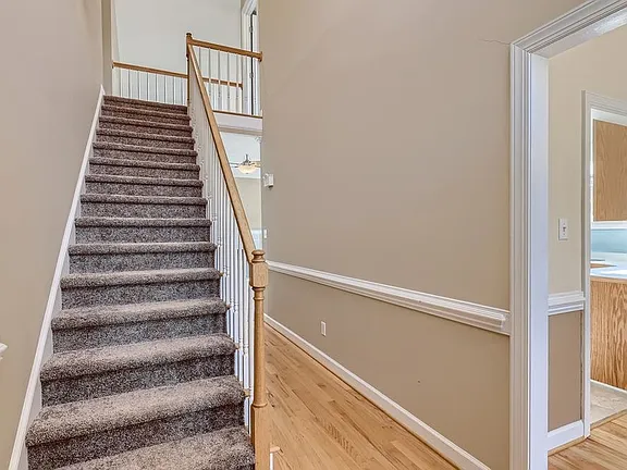 Entry hall with warm wood flooring, a carpeted staircase, and white chair rail trim