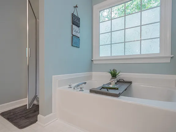 Light blue bathroom with a soaking tub, glass shower, and a broad frosted window