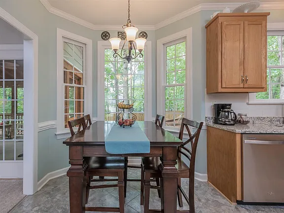 Breakfast area with tall windows, warm wood furniture, and an opening to the screened porch