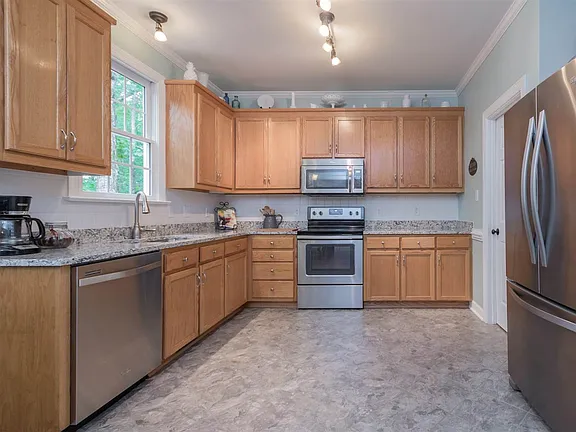 Kitchen with warm wood cabinetry, stone counters, stainless appliances, and track lighting