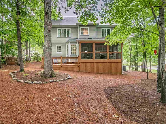 Rear view of the gray home with a screened wood porch surrounded by mature trees