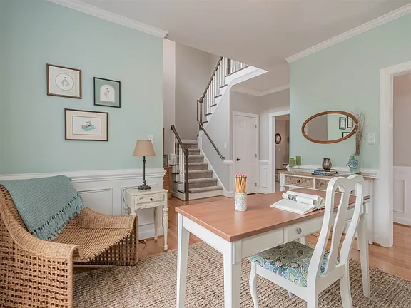 Soft blue study with white wainscoting, warm wood flooring, and a view toward the staircase