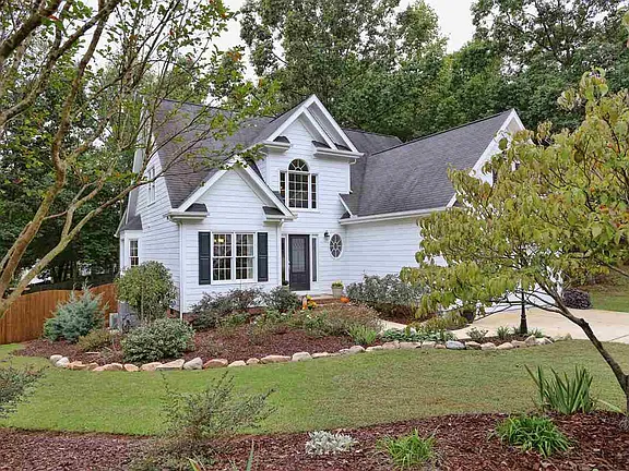 Angled exterior view of a white gabled home framed by mature landscaping