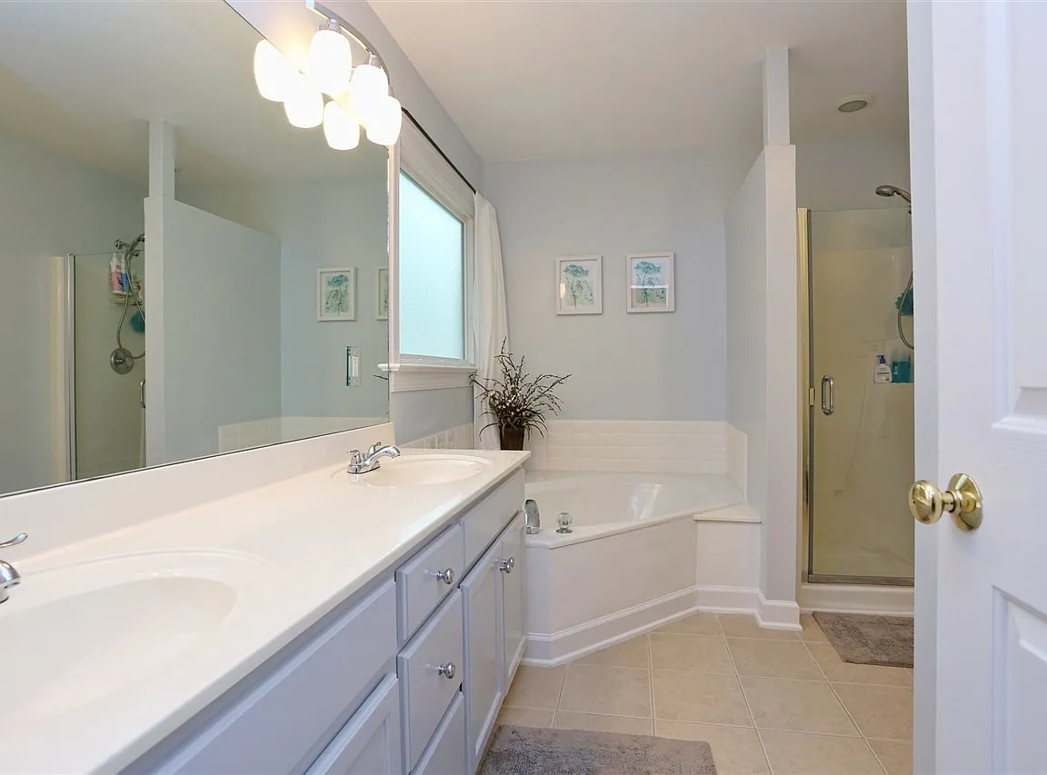 Bright bathroom with a double vanity, corner soaking tub, and glass-enclosed shower