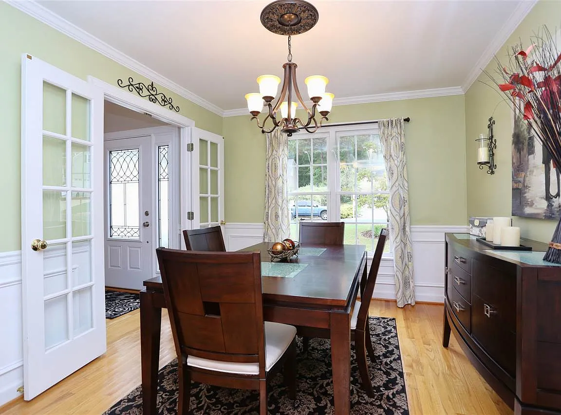 Light green dining room with French doors, white wainscoting, and warm wood flooring