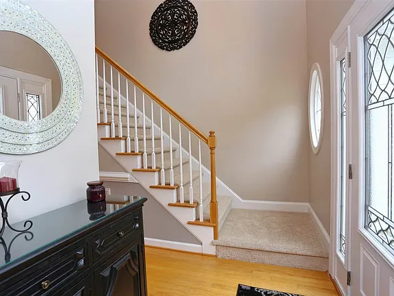 Bright entry hall with warm wood flooring, a white staircase, and decorative glass doors