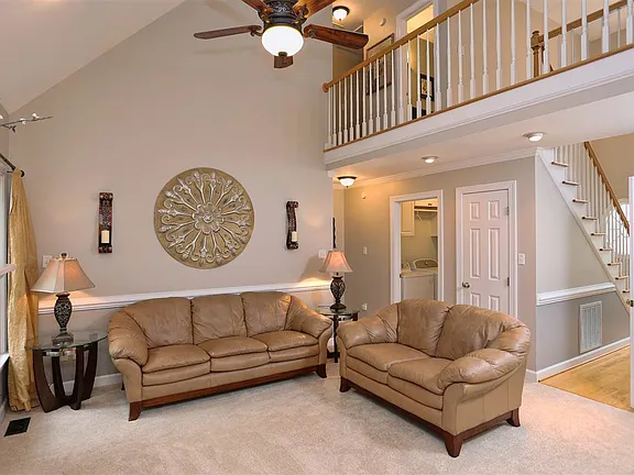 Open great room with a vaulted ceiling, upper-level railing, and neutral furnishings