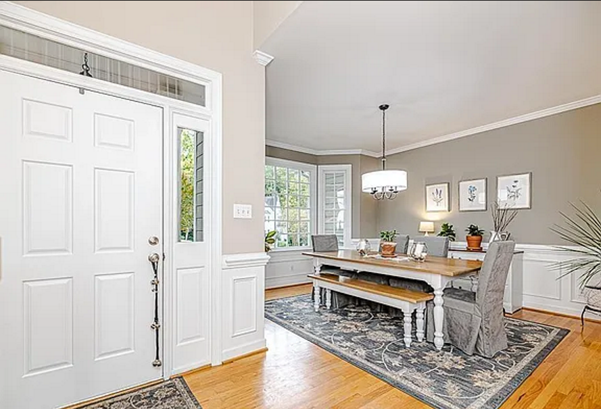 Dining room with white wainscoting, a bay window, warm wood flooring, and a long gathering table