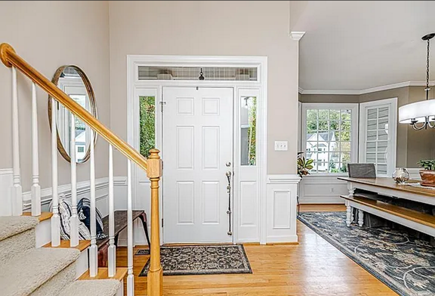 Bright entry hall with warm wood flooring, a white staircase, and a view into the dining room