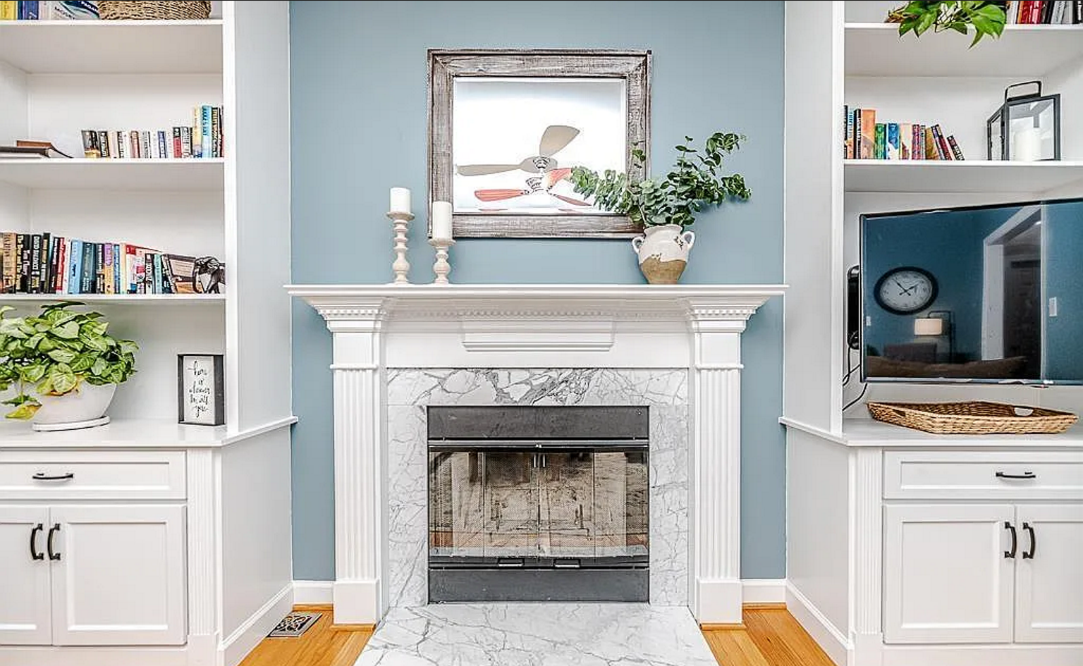 White fireplace with a marble surround, blue accent wall, and built-in cabinetry