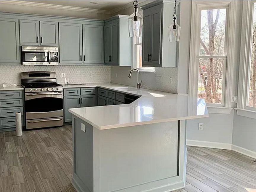 Kitchen with muted blue cabinetry, white counters, pendant lighting, and tall bay windows