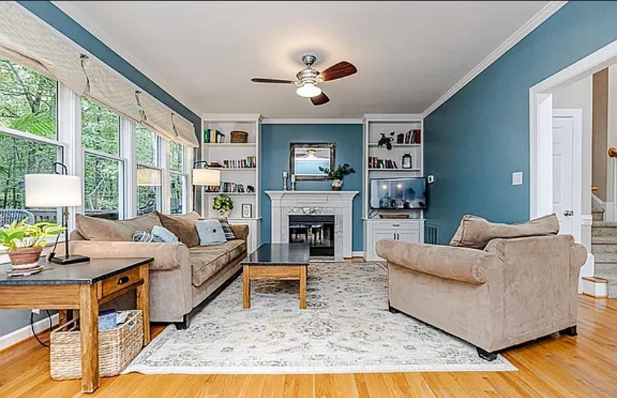 Blue living room with a white fireplace, built-in shelving, broad windows, and neutral furnishings
