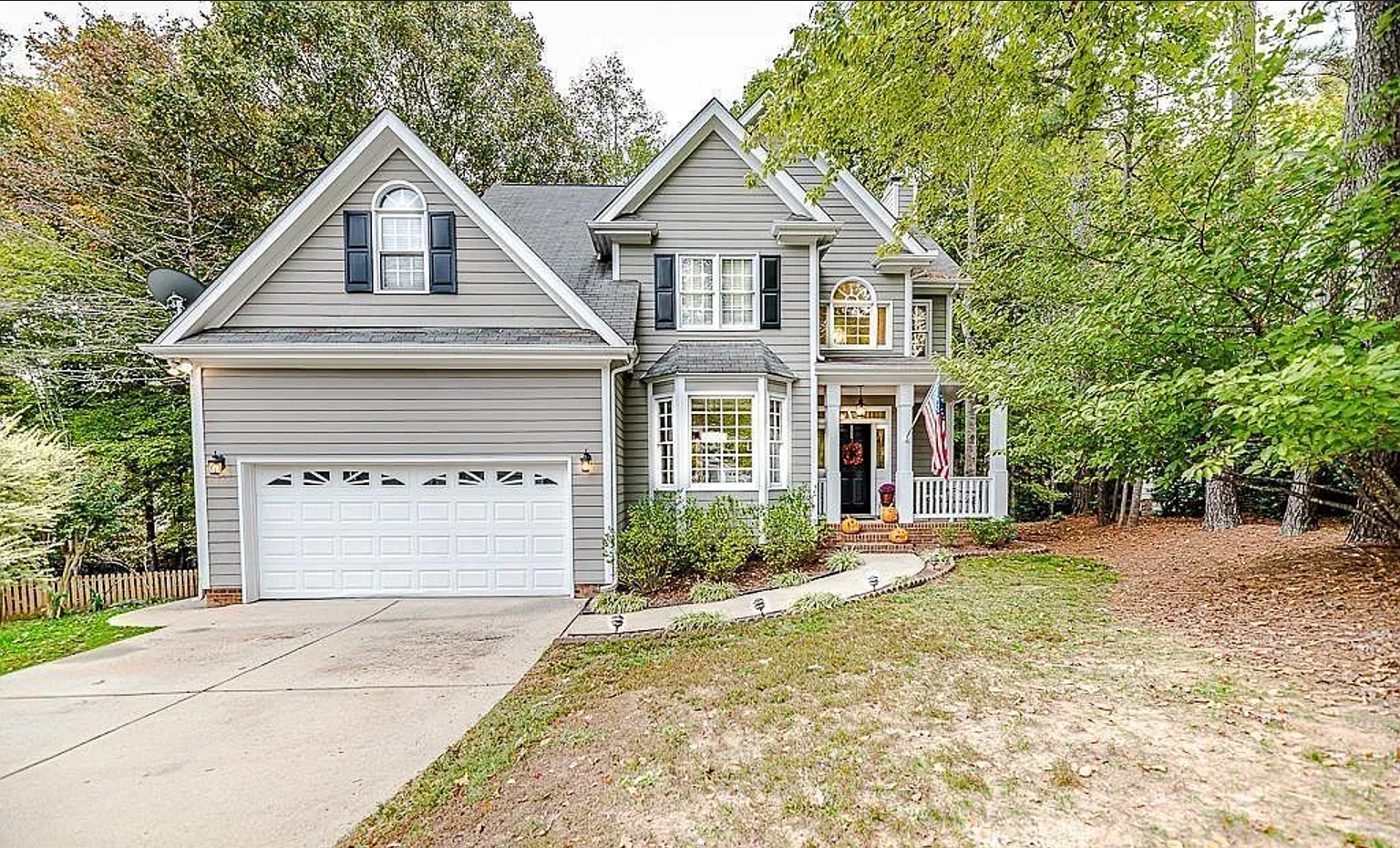 Two-story gray home with layered gables, a projecting bay, covered entry, and wooded setting