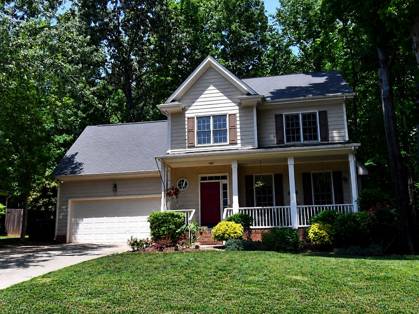 Two-story gray home with a red front door, broad covered porch, and wooded setting