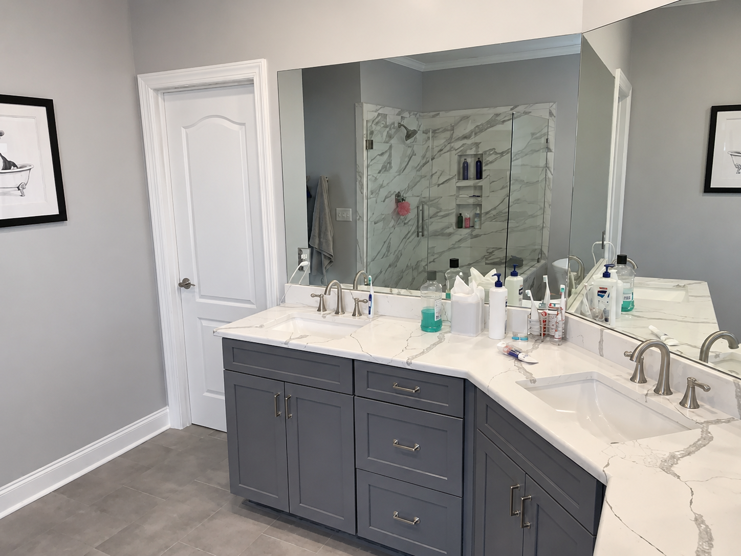 Gray double vanity with marble-look counters and a mirrored view of the shower