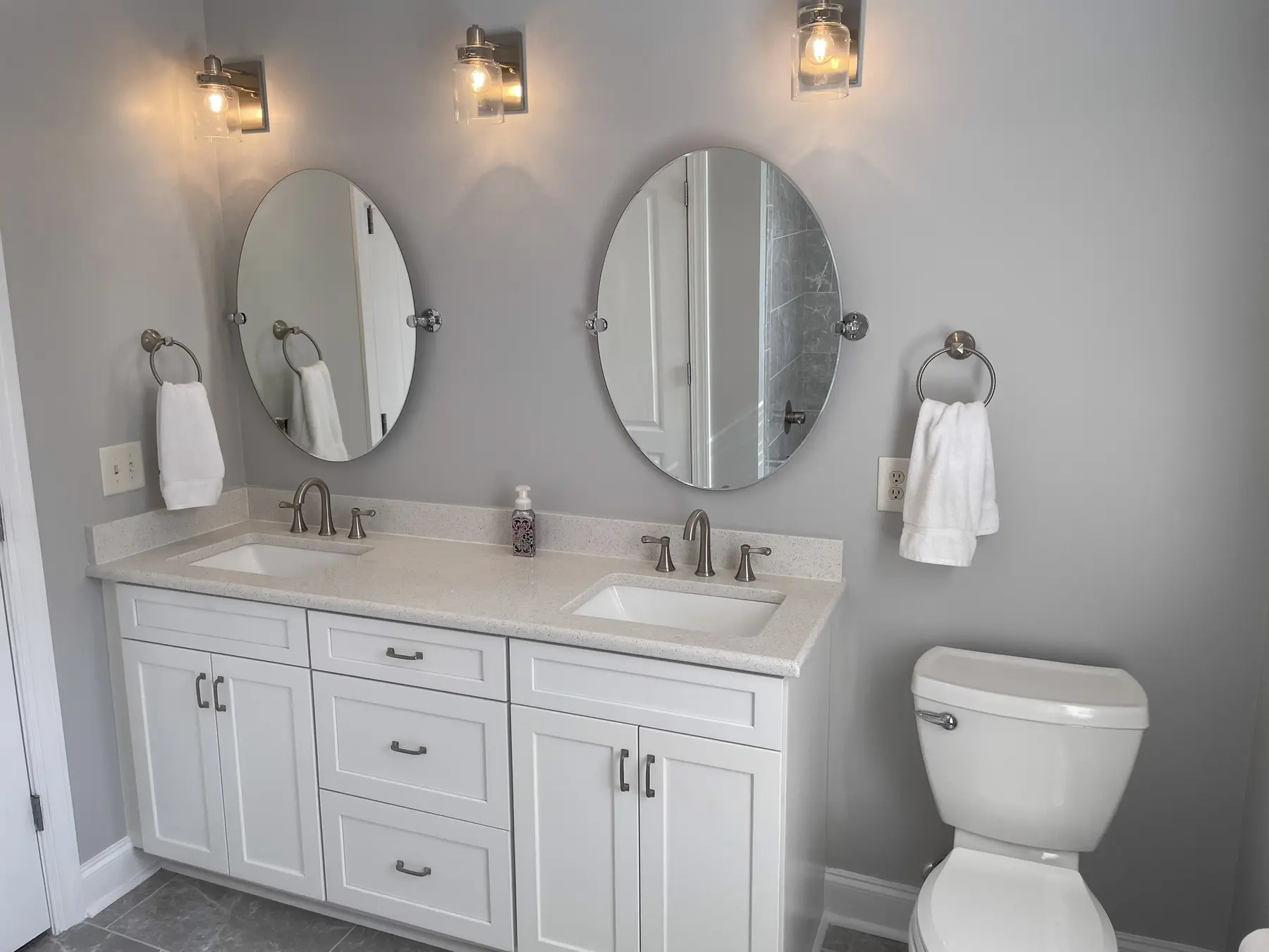 Bright renovated bathroom with white double vanity and oval mirrors
