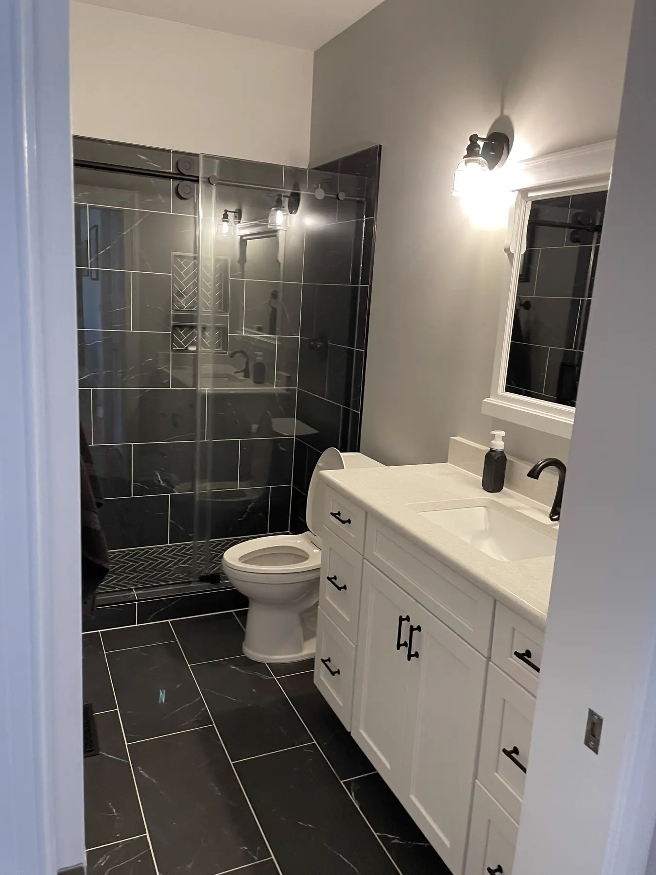 Compact bathroom with dark tiled shower and white vanity