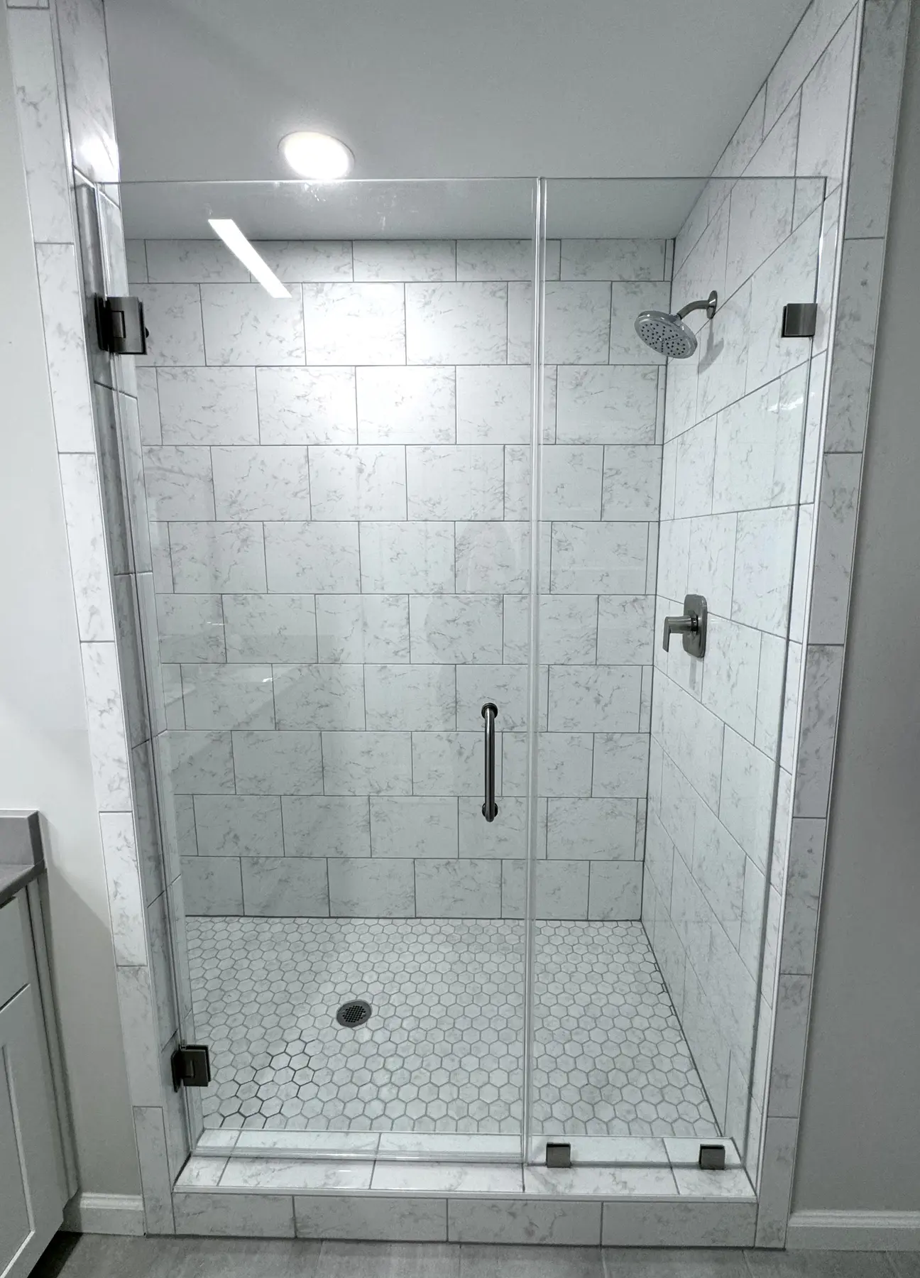 Frameless glass shower with marble-look tile and hexagonal floor tile