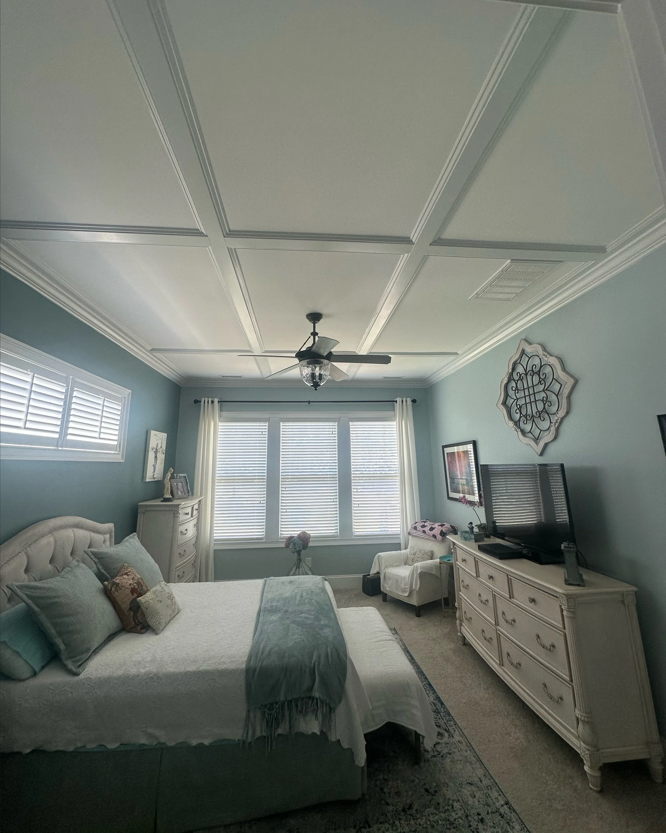 White coffered bedroom ceiling with layered trim and a central ceiling fan
