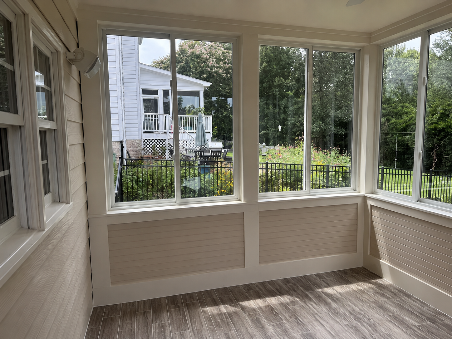 Finished sunroom interior with corner windows, paneled lower walls, and garden views